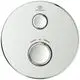 Rundes Duschthermostat der Marke Ideal Standard in Chrom mit zwei Drehknöpfen zur Temperatur- und Wassermengenregulierung, montiert auf einer glatten Oberfläche.